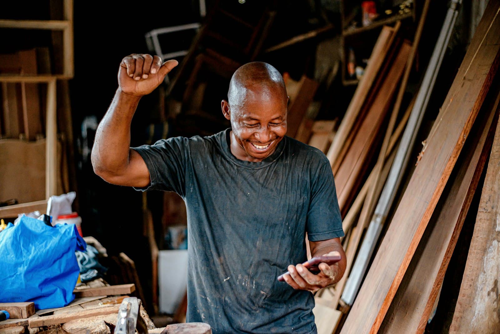 A man in his workshop smiling and celebrating as he reads good news on his phone